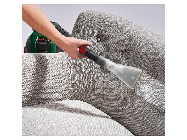 Main nettoyant un canapé en tissu gris avec un outil de nettoyage de rembourrage.