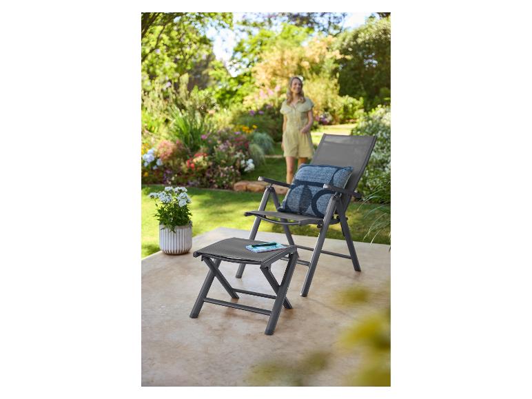 Chaise de jardin grise et repose-pieds sur une terrasse avec une femme en arrière-plan.