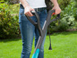 Une femme tient une débroussailleuse électrique Gardena dans un jardin.