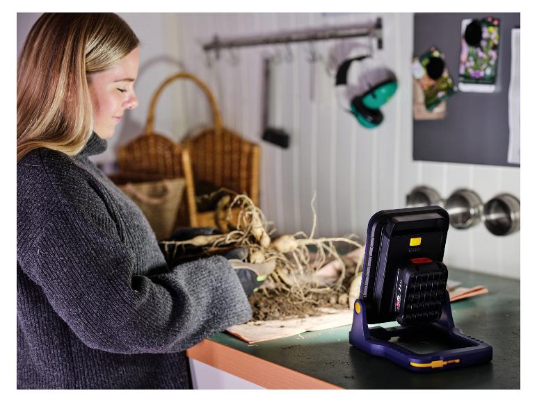 Femme plantant des plantes avec une lampe de travail LIVARNO® 18 V »BWL2400 P4A« éclairant la zone de travail.