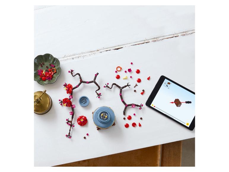 Pièces de construction de fleurs de cerisier et tablette avec instructions sur une table blanche.