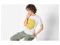 Une femme porte un t-shirt blanc avec un imprimé floral et un pantalon vert.