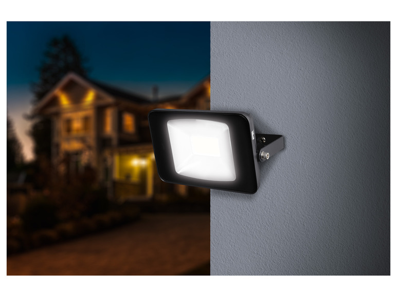 Un projecteur LED noir monté sur un mur, avec une maison en arrière-plan.