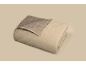 Couverture matelassée beige pliée avec un côté intérieur gris-brun et des coutures en losange.