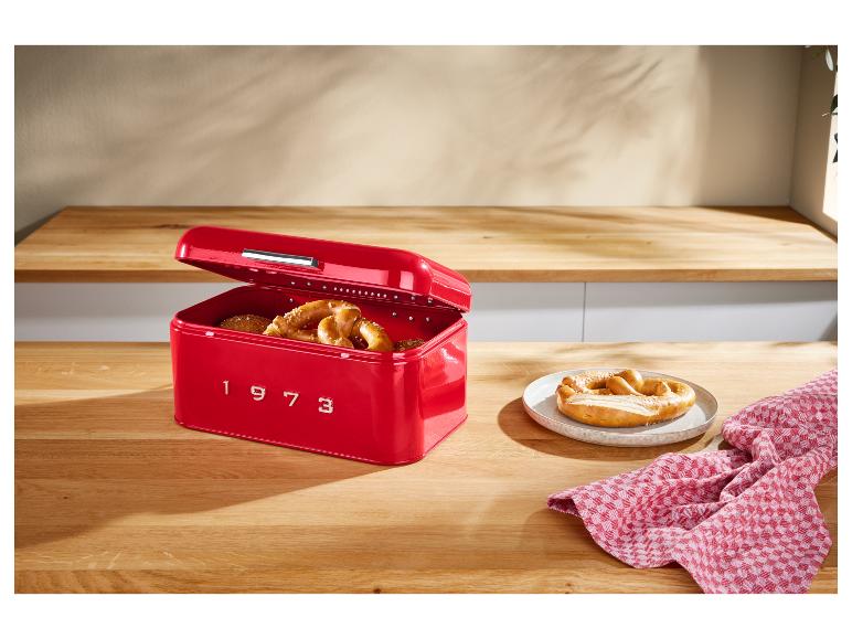 Une boîte à pain rouge en métal avec le numéro '1973' sur une table en bois avec des bretzels.