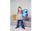Fille souriante tenant une peluche bleue, debout dans un salon.