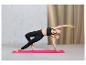 Une femme fait du yoga sur un tapis rose, portant un legging noir et un soutien-gorge de sport.