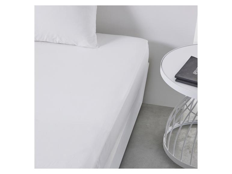 Draps blancs sur un lit avec une table de chevet blanche.