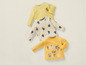 Trois t-shirts à manches longues pour bébé : un jaune avec un ours, un blanc avec des bateaux et un jaune avec le texte 'travel the world'.