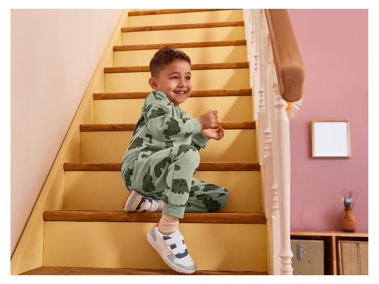 Garçon souriant en survêtement vert dinosaure assis sur les escaliers.