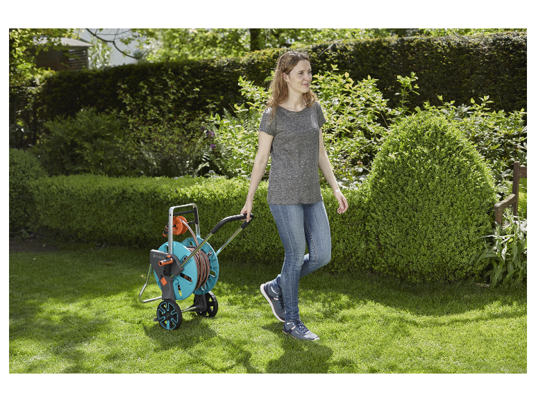 Une femme promène un dérouleur de tuyau d'arrosage Gardenena dans son jardin.