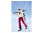 Une femme en pantalon de ski rouge et un casque blanc Crivit marche dans la neige avec du matériel de ski.