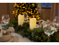Table de Noël décorée de bougies, guirlande de houx et de pin, et sapin de Noël illuminé en arrière-plan.