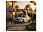 Voiture blanche sous un carport moderne avec toit transparent, dans un jardin paysager au coucher du soleil.