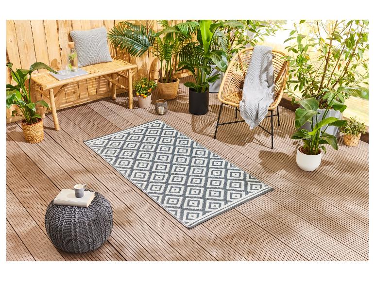 Tapis d'extérieur géométrique, mobilier de jardin en rotin et plantes vertes.