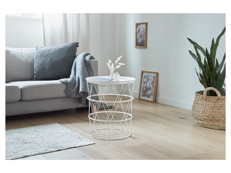 Une table d'appoint blanche en métal avec un panier en osier à côté.