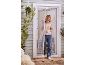 Femme souriante traversant un rideau de porte moustiquaire blanc vers une terrasse.