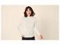 Femme souriante portant un pull à col roulé côtelé blanc cassé et un pantalon noir.