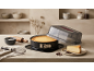 Cheesecake dans un moule à charnière avec couvercle, ustensiles de pâtisserie et une part de gâteau.