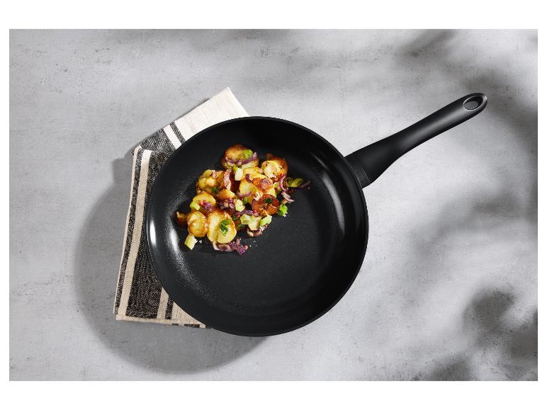Une poêle à frire noire avec des pommes de terre frites, des oignons rouges et des herbes vertes sur une surface grise.