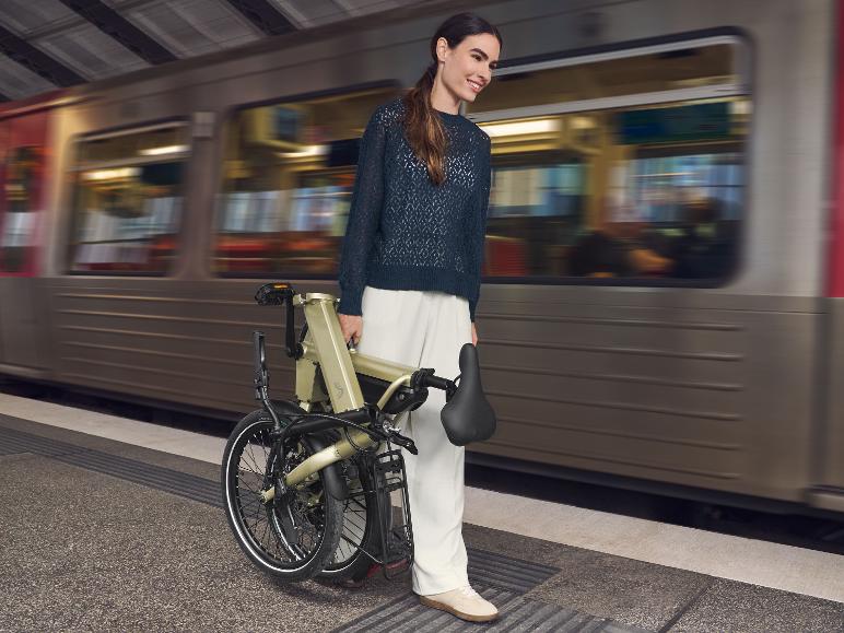 Femme tient un vélo pliant dans une gare pendant qu'un train passe.