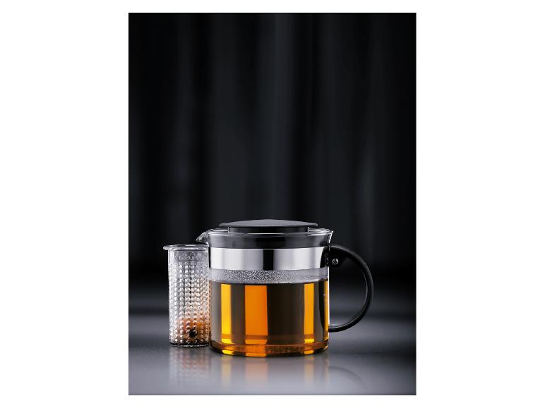 Théière en verre avec infuseur, remplie de thé ambré.