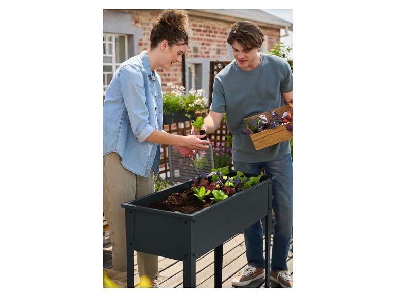Un couple plantant des semis de laitue dans une jardinière surélevée sur un balcon.