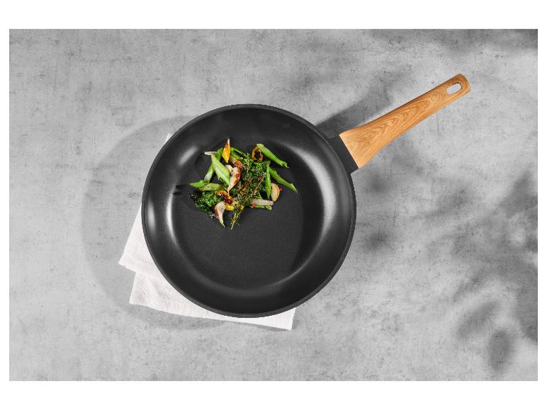 Poêle à frire avec manche en bois, avec légumes sautés sur un linge blanc sur une surface en ciment.