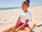 Une fille portant un t-shirt blanc avec l'inscription 'Fresh Summer' assise sur la plage.