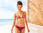 Une femme en bikini rose à imprimé tropical sur la plage.