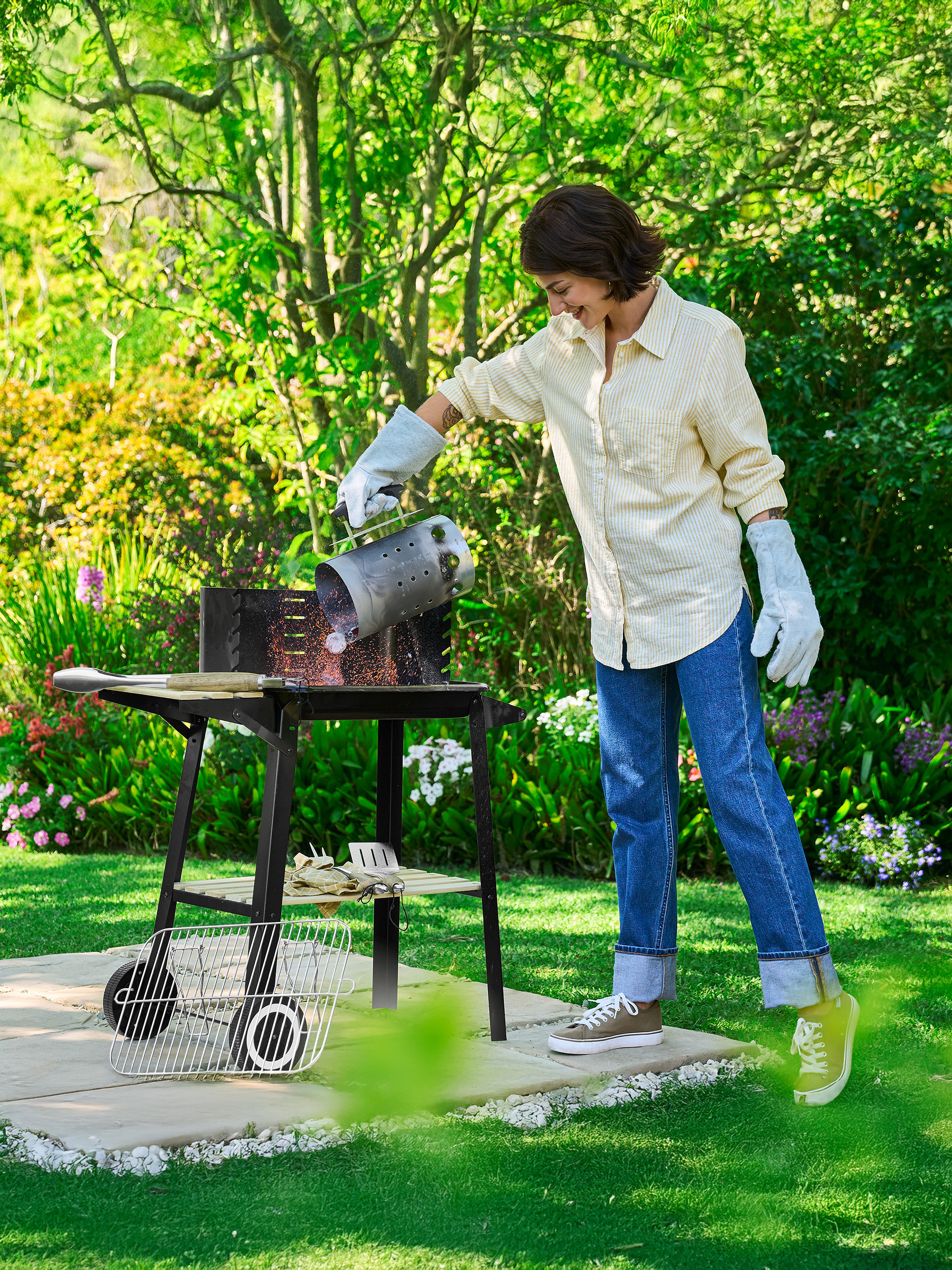 Femme versant du charbon d'une cheminée d'allumage dans un barbecue extérieur.