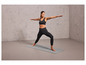 Une femme en soutien-gorge de sport noir et en leggings fait du yoga sur un tapis gris.