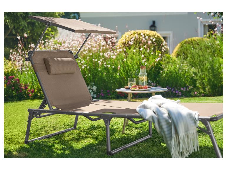 Chaise longue avec pare-soleil dans le jardin, avec boissons et fruits sur la table.