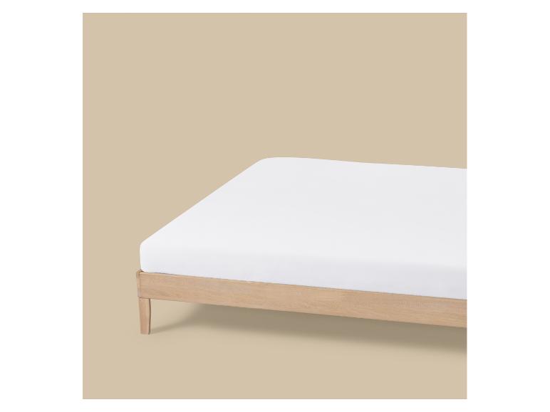 Drap-housse blanc sur un cadre de lit en bois clair.