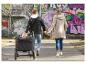 Famille avec enfant en poussette se promène main dans la main le long d'un mur de graffitis.