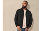 Un homme portant une veste noire, un t-shirt beige et un jean bleu.