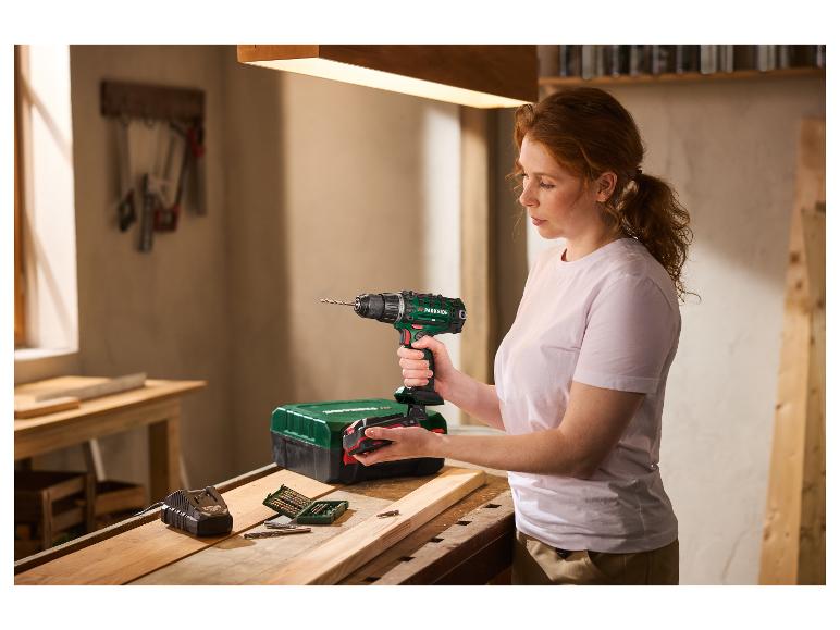 Une femme insère une batterie dans une perceuse-visseuse sans fil PARKSIDE 20 V sur un établi