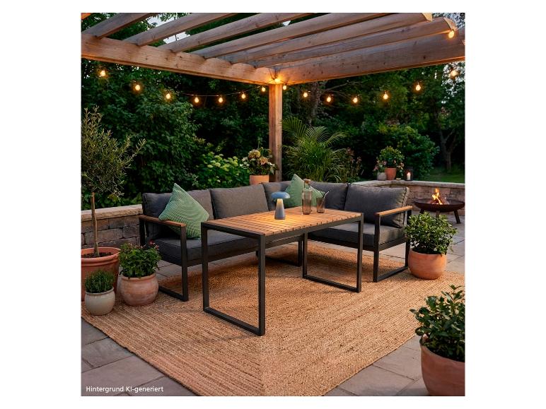 Salon de jardin avec table en bois, canapés gris foncé et guirlandes lumineuses sous une pergola.