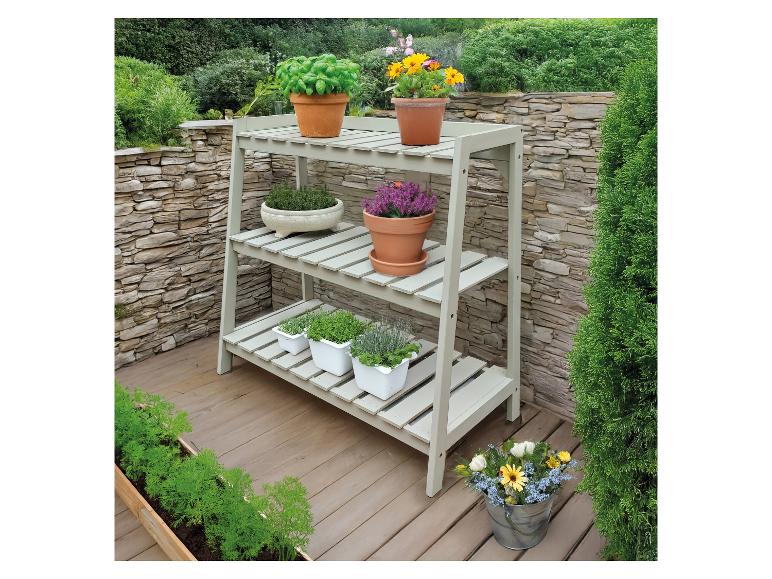 Étagère en bois à trois niveaux remplie de diverses plantes et fleurs sur une terrasse.