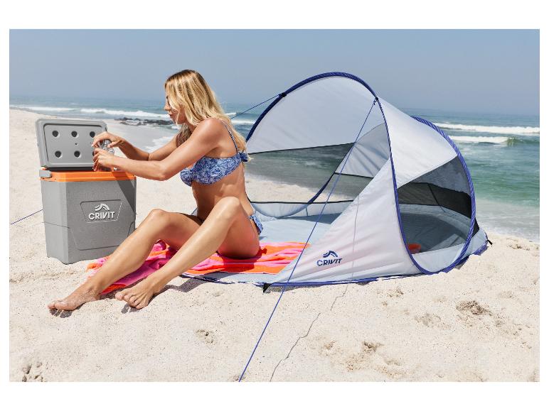 Femme sur la plage assise près d'une tente et d'une glacière, ouvrant une bouteille.