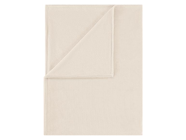 Plaid en polaire beige, partiellement plié, montrant sa texture douce.
