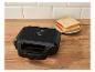 Appareil à sandwich noir avec voyants lumineux et deux tranches de pain sur une assiette.