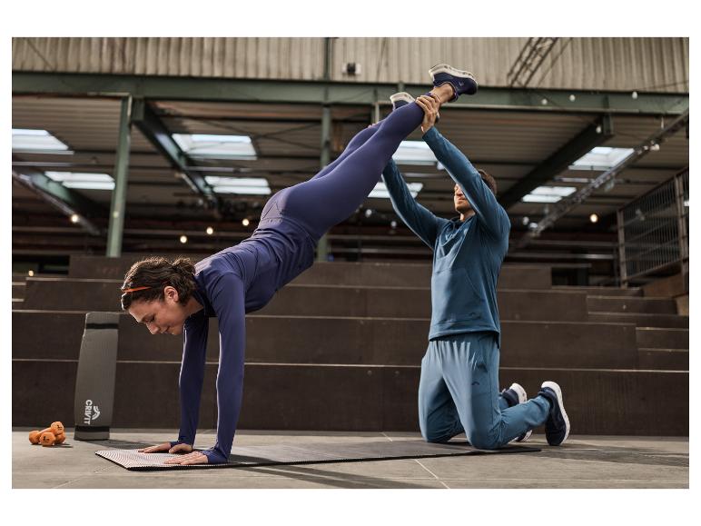 Femme portant des chaussures de sport CRIVIT faisant le poirier avec l'aide d'un partenaire.