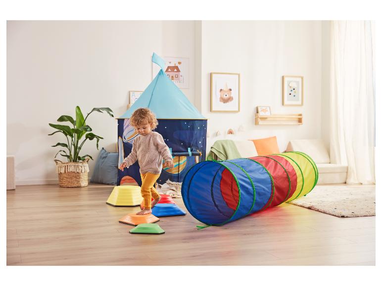 Enfant jouant avec des pierres d'équilibre colorées et un tunnel dans une chambre d'enfant avec tente de jeu.