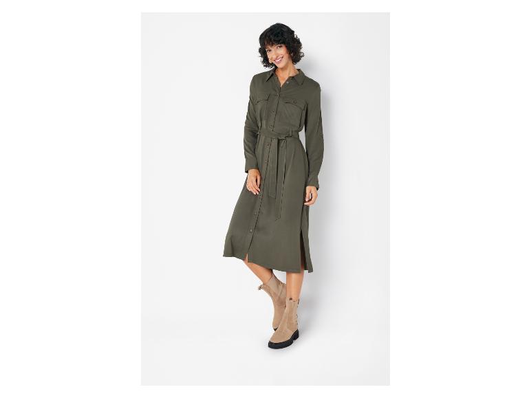 Une femme porte une robe chemise verte avec une ceinture et des bottines marron.