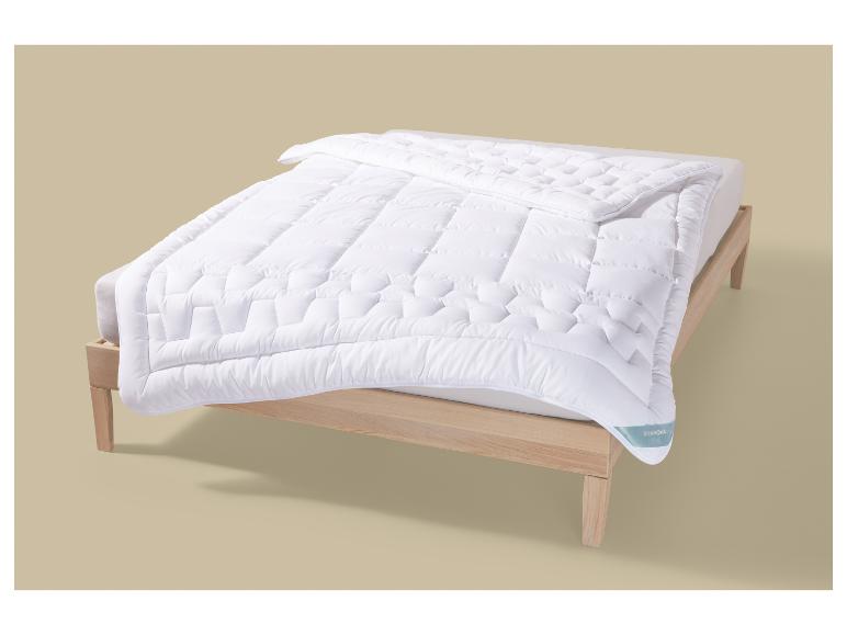 Couette blanche matelassée sur un lit en bois, avec l'étiquette Stargill visible.