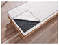 Un matelas blanc avec un surmatelas gris, visible sur un sommier à lattes en bois.