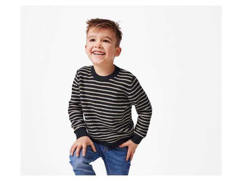 Un garçon souriant portant un pull rayé et un jean.