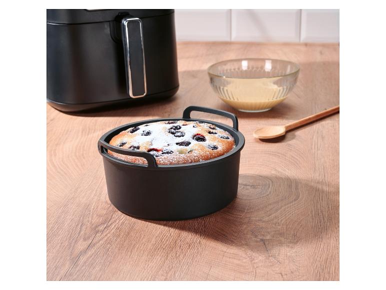 Gâteau aux fruits dans un moule en silicone pour friteuse à air, à côté d'une friteuse et d'un bol de liquide.