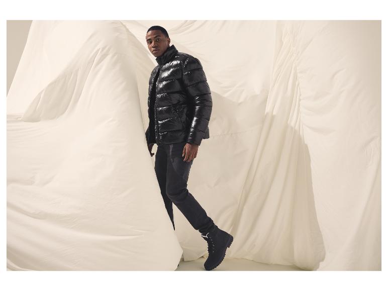 Homme en doudoune noire brillante et jean foncé devant un tissu blanc.